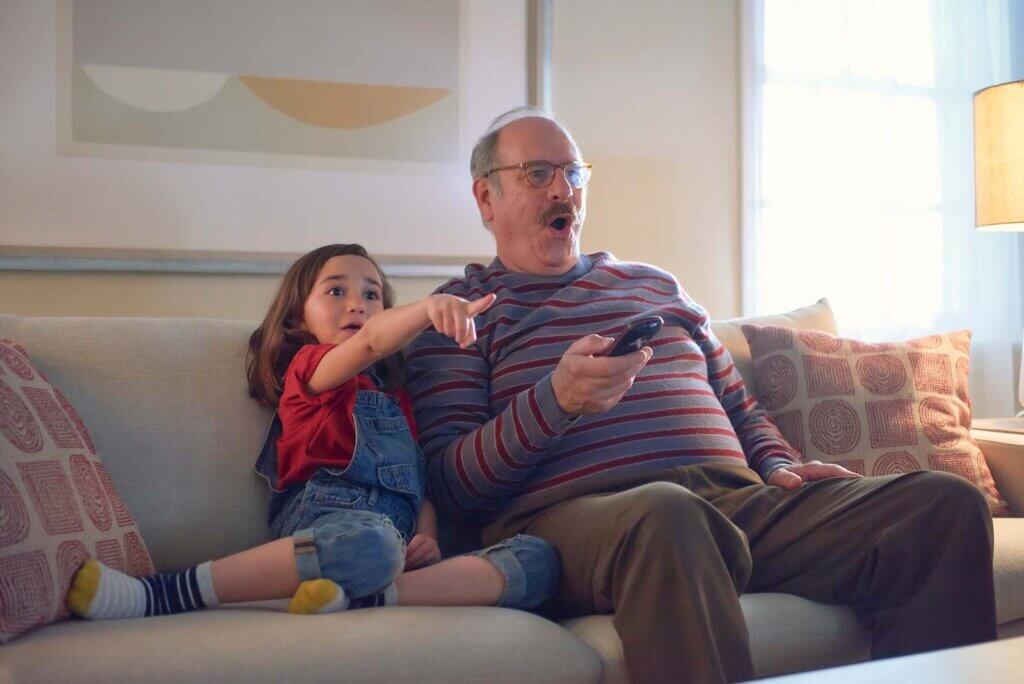 older man and young girl watch kids TV on their couch