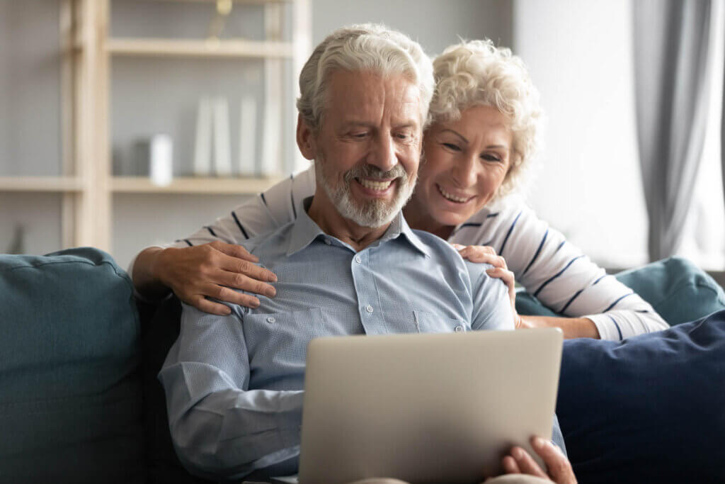 elderly couple sitting on couch while using a laptop