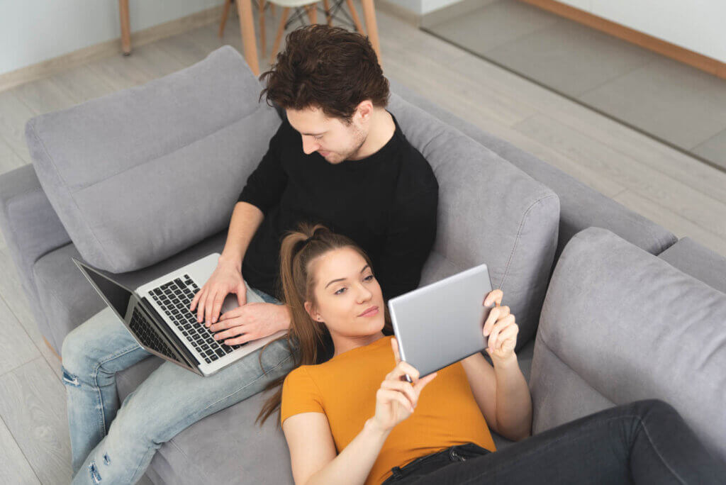 Couple using fast home internet with laptop and digital tablet. Woman and man on sofa in living room