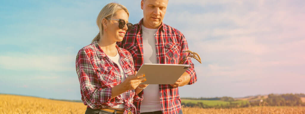 una joven pareja sonríe mientras comparte su dispositivo digital en un campo rural