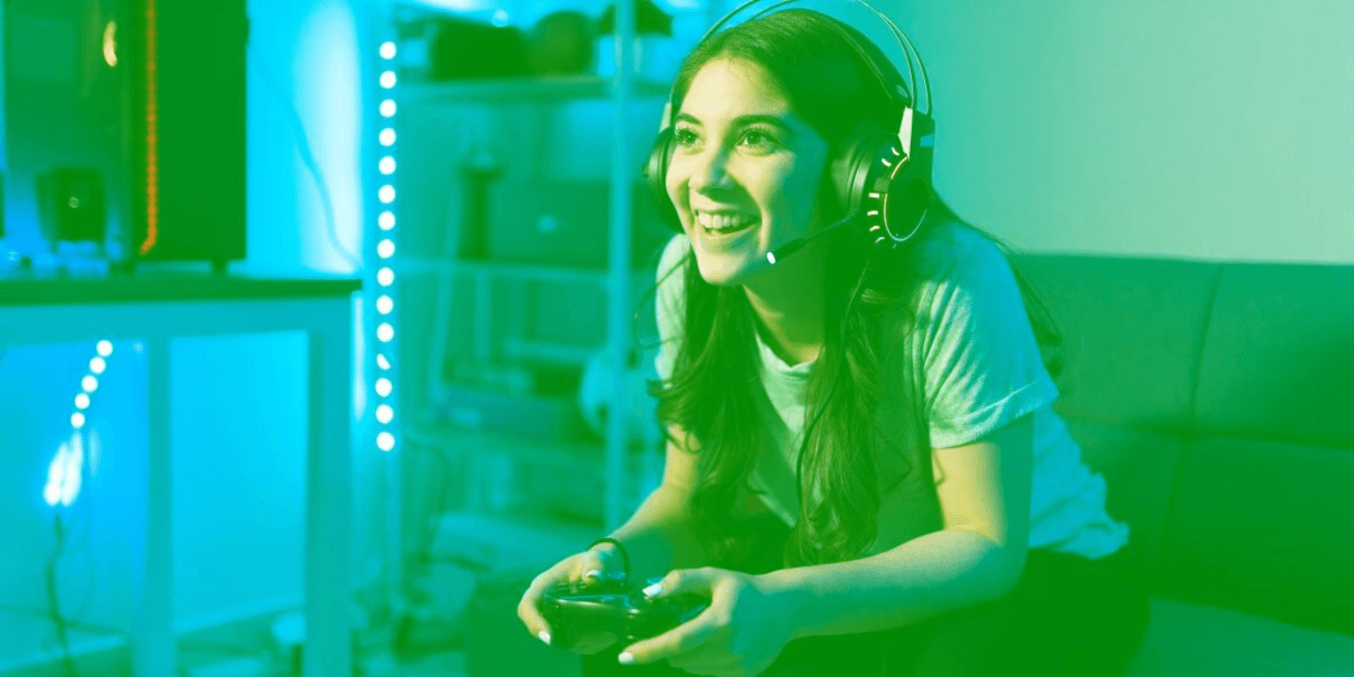 Chica sonriendo con mando de juego en mano mientras juega en tiempo real en casa
