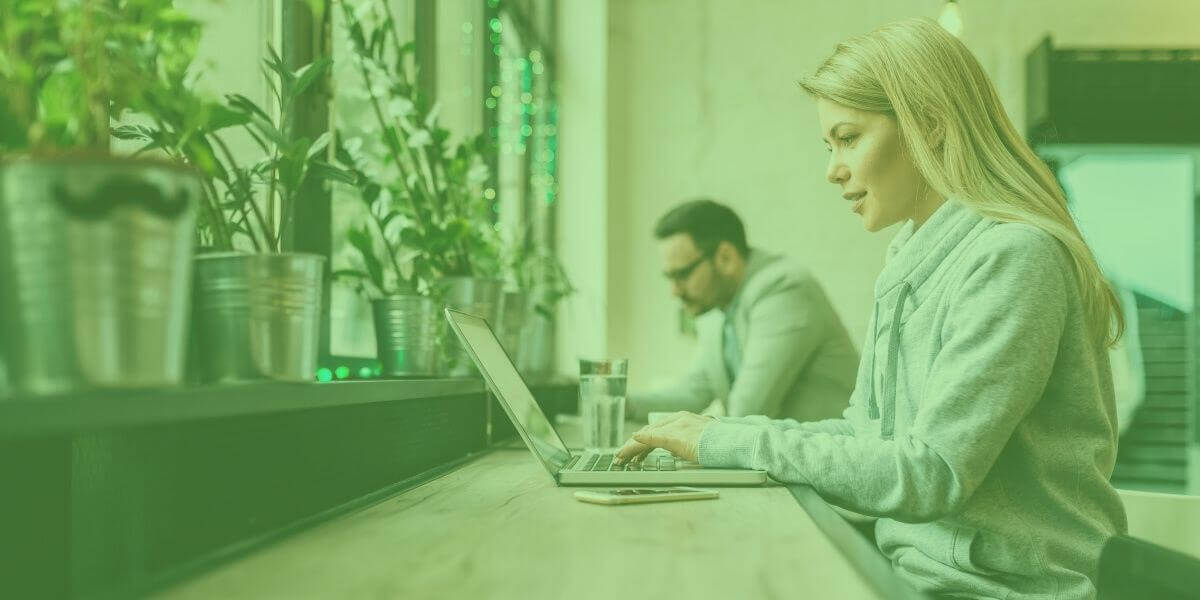 A blond woman protects her private information while sitting in a cafe with her digital device