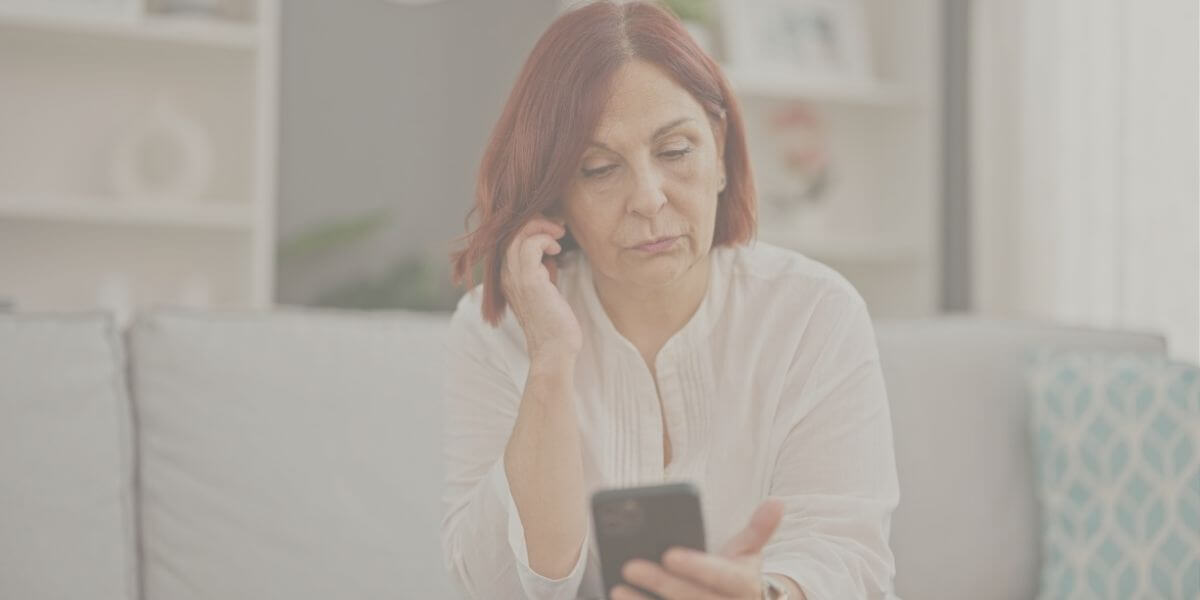 Una mujer de mediana edad parece frustrada mientras usa su smartphone en casa