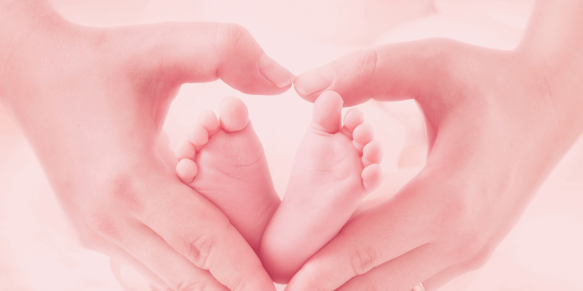 Pies de bebé con las manos de mamá formando un corazón