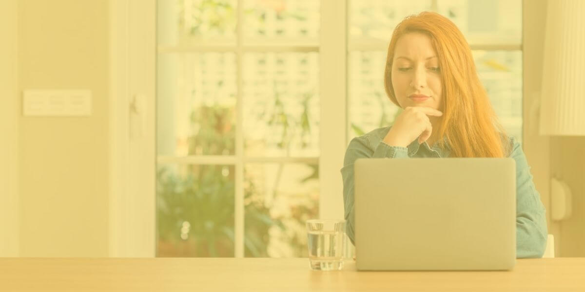 Red-haired woman looks seriously at her home laptop screen