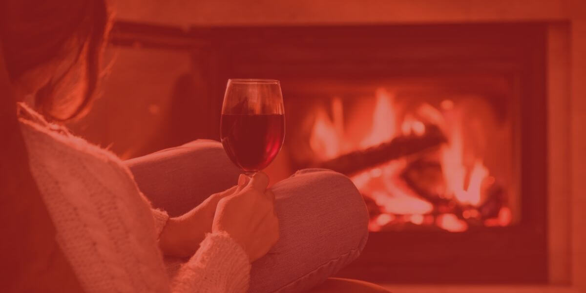 woman sits in front of fireplace with wine