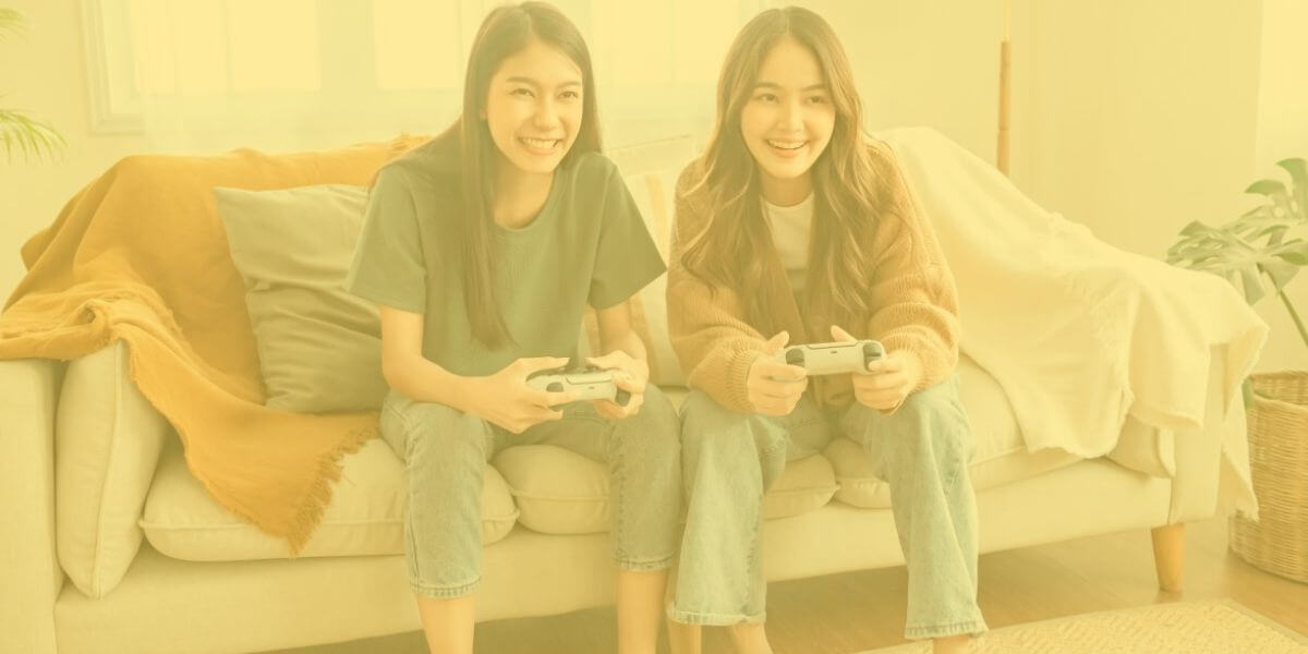 Two roommates sit on a couch holding gaming controllers