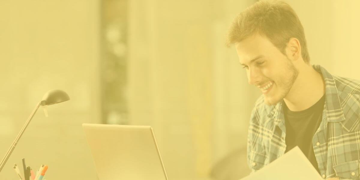 male student smiles while using his laptop at home