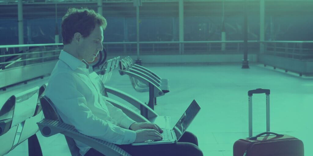 man sitting in airport terminal with luggage using Wi-Fi