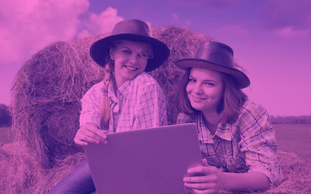 two girls using a laptop in a hayfield