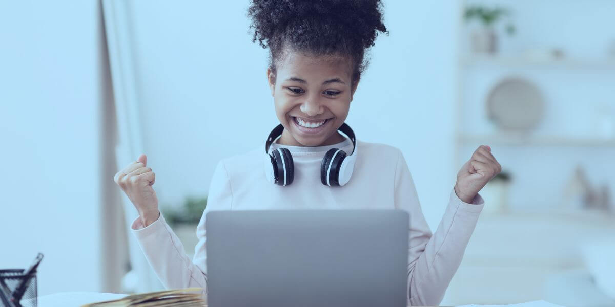 young girl wearing headphones while smiling, using her laptop for online learning