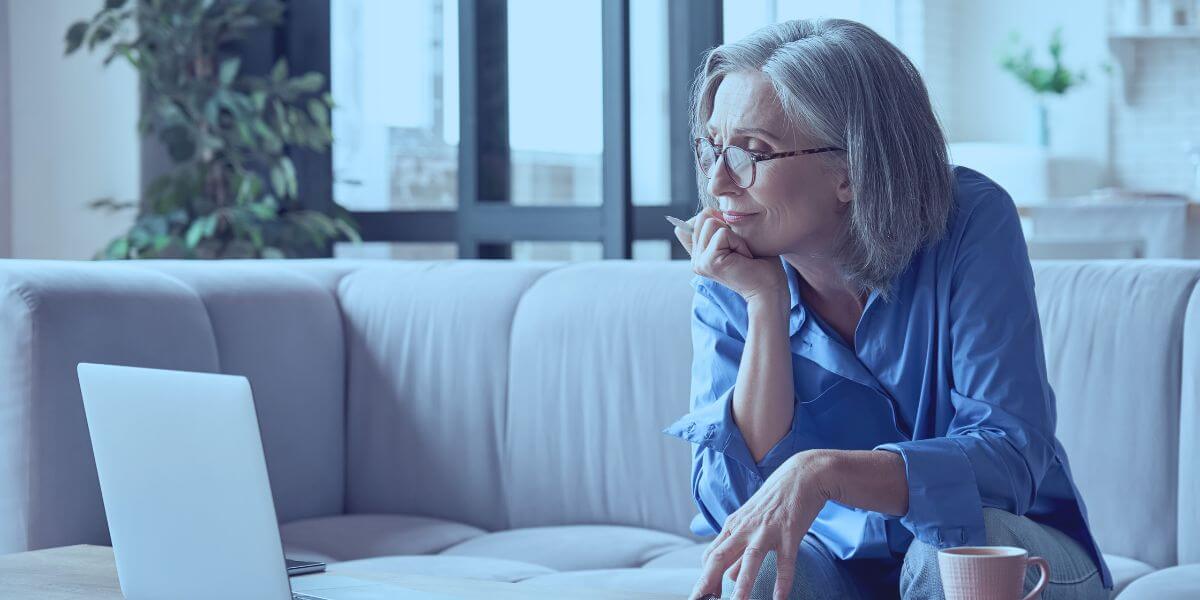 older woman sitting on the couch with her laptop and a cup of tea using online learning platform