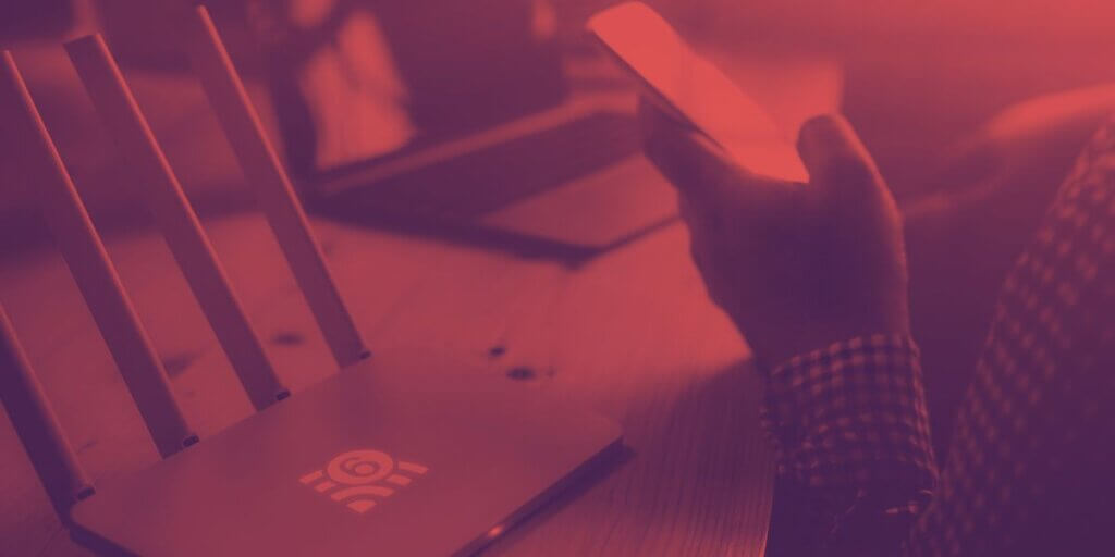 Router sitting on desk next to person holding cell phone and a laptop in background