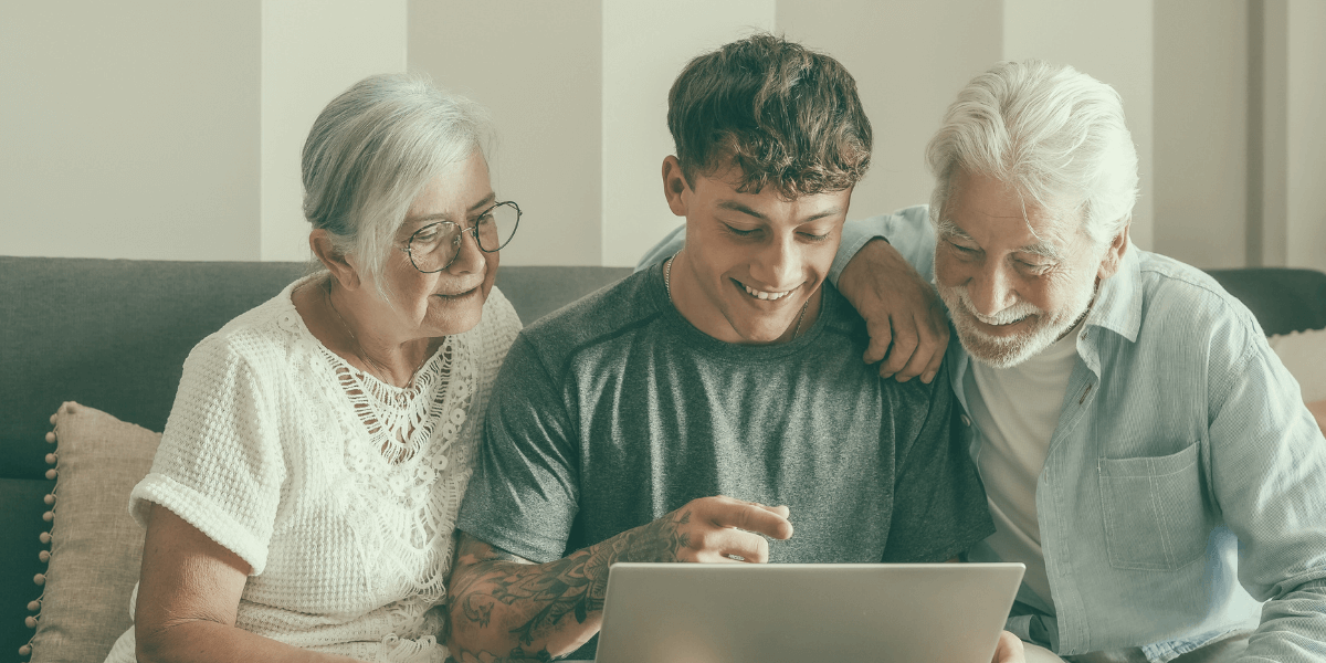 young man helping older man and woman on their laptop