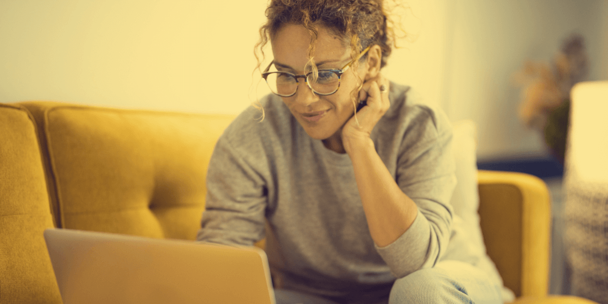 a woman smiling while sitting on the couch using her laptop