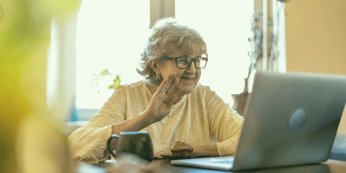 woman with glasses waving at a laptop on video call