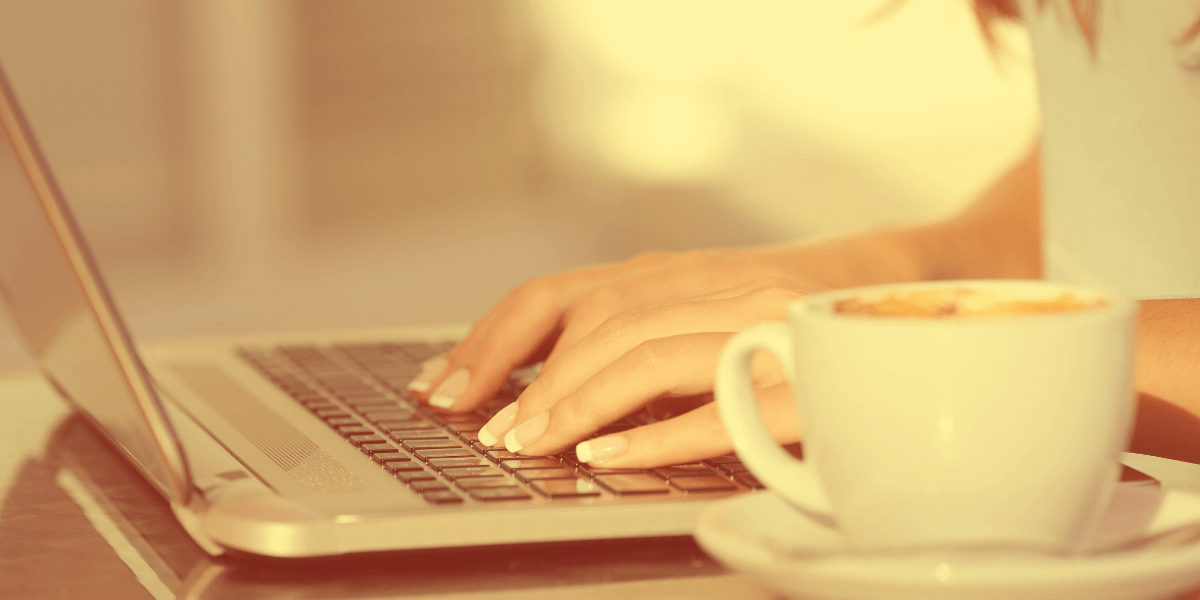 person typing on a laptop with a cup of coffee nearby