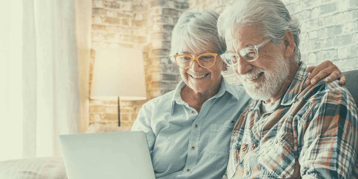 white haired man and woman smiling while using a laptop