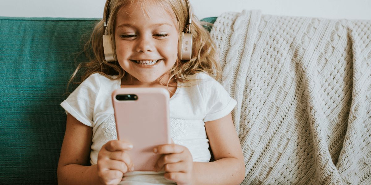 little girl wearing headphones smiling at her phone