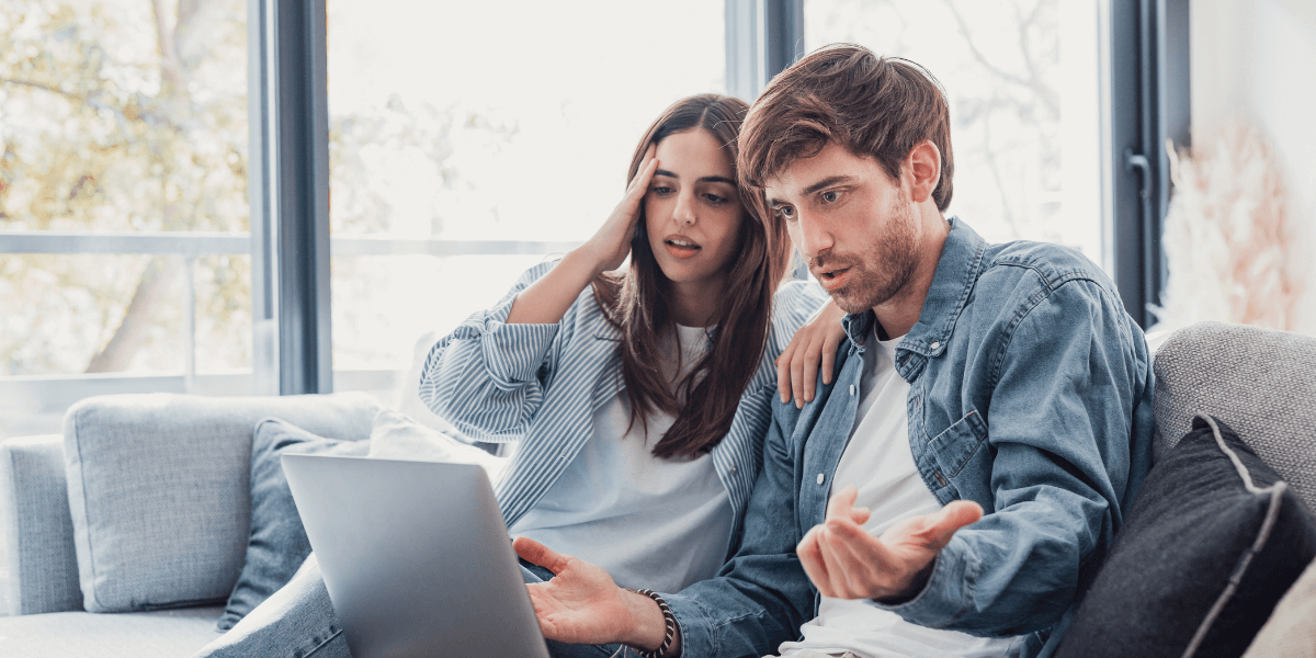 Man and woman looking at a computer in distress while holding a paper