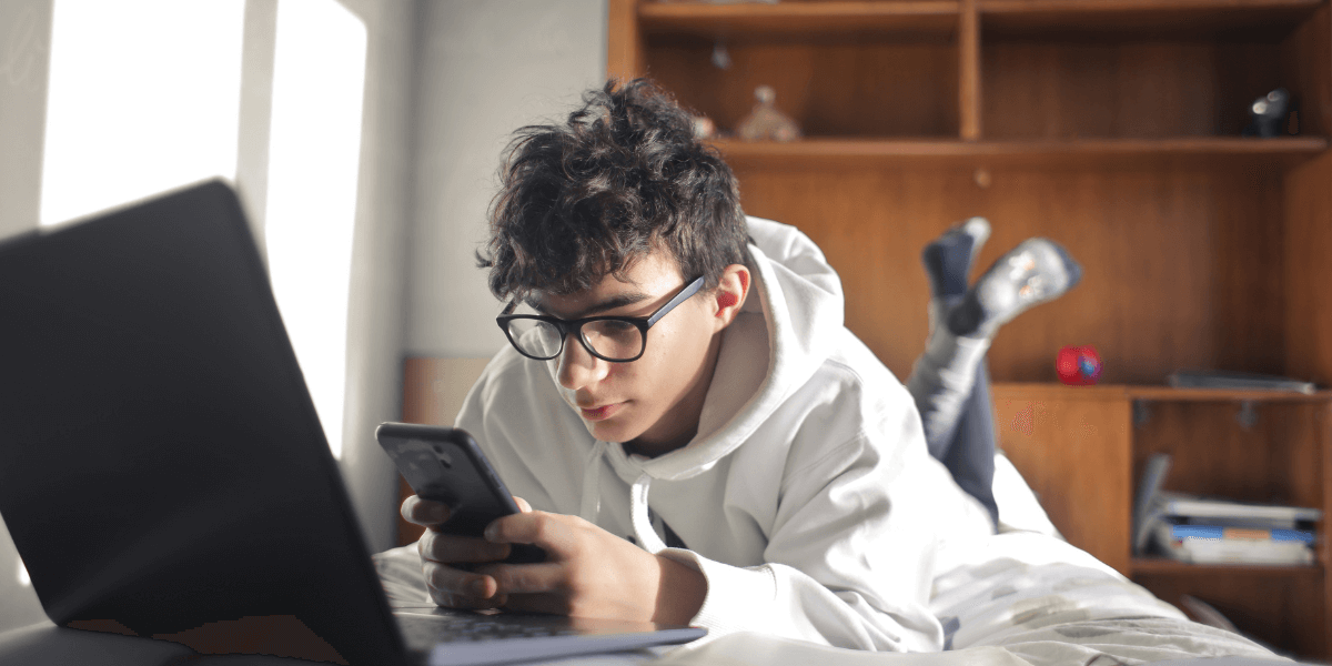 Young boy on his bed with his phone and laptop out