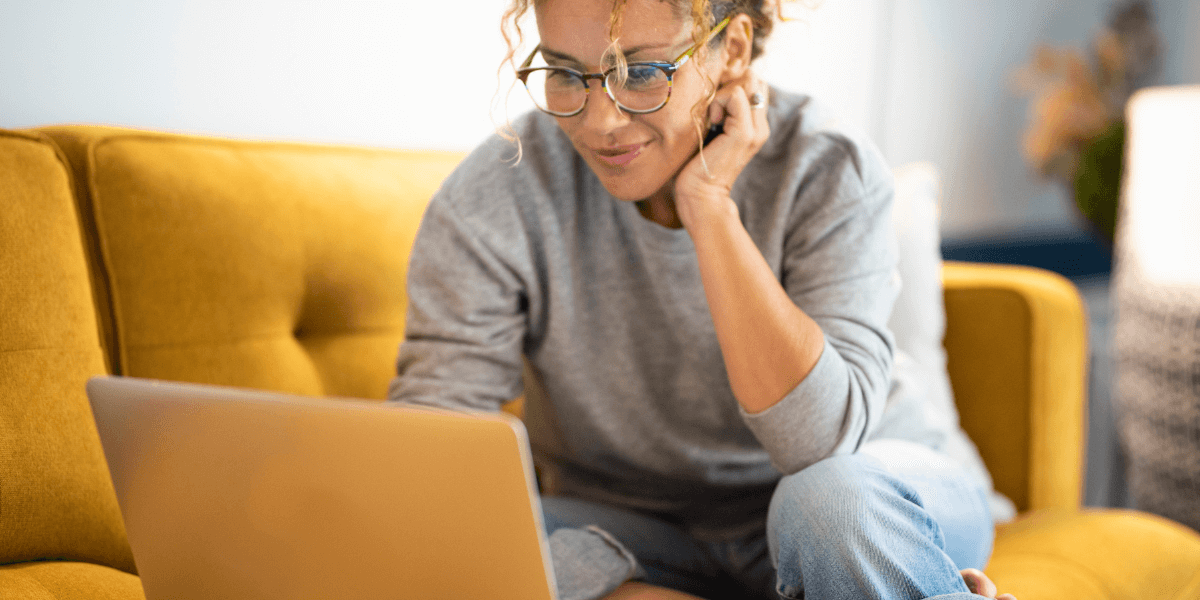 Woman on a yellow couch looking at her laptop