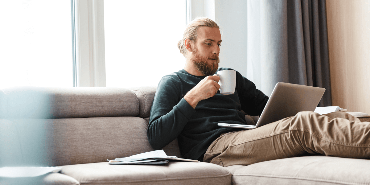 Man drinking coffee the couch while looking at his laptop