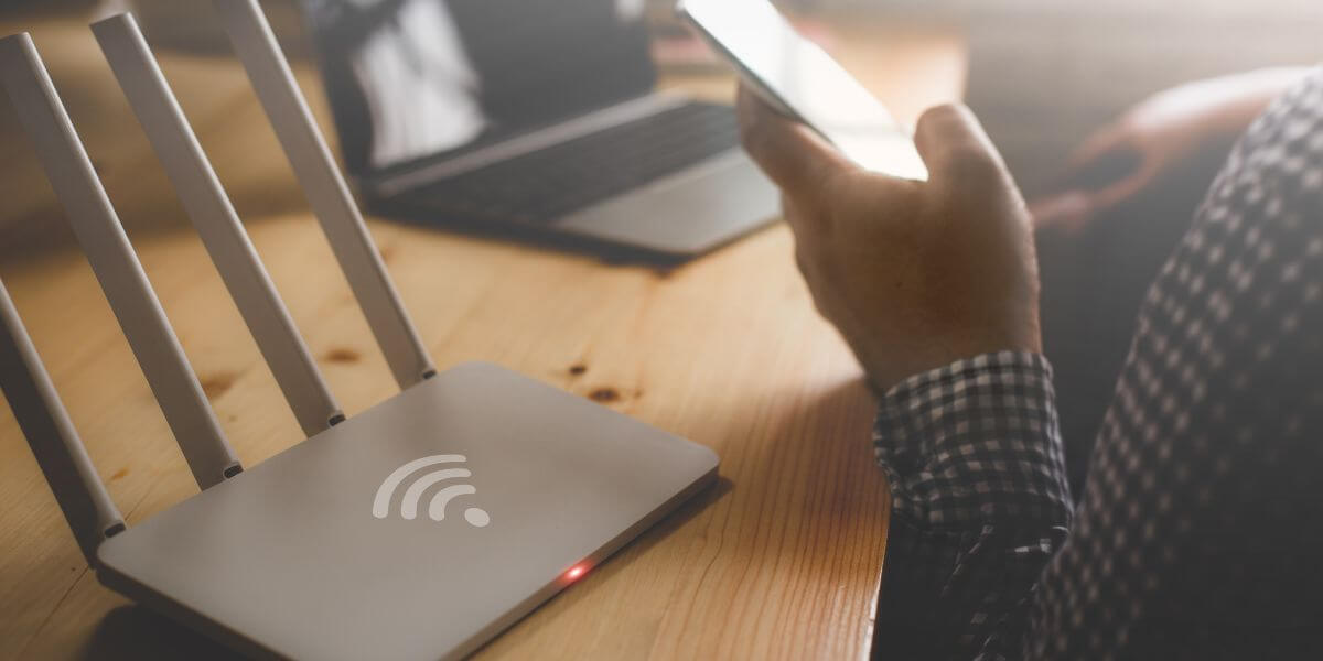 person on phone next to laptop and router