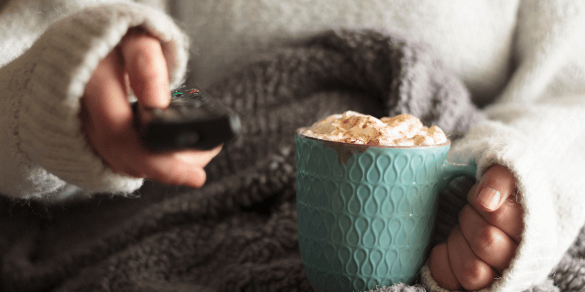 person holding hot chocolate and a tv remote