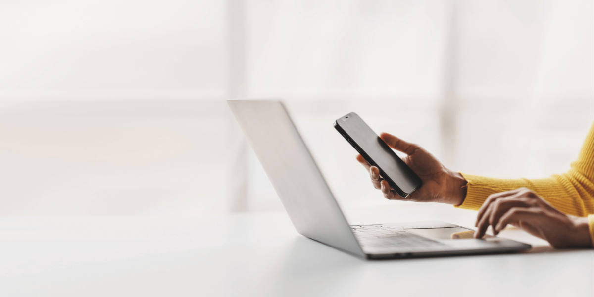 hand holding a phone and typing on a laptop