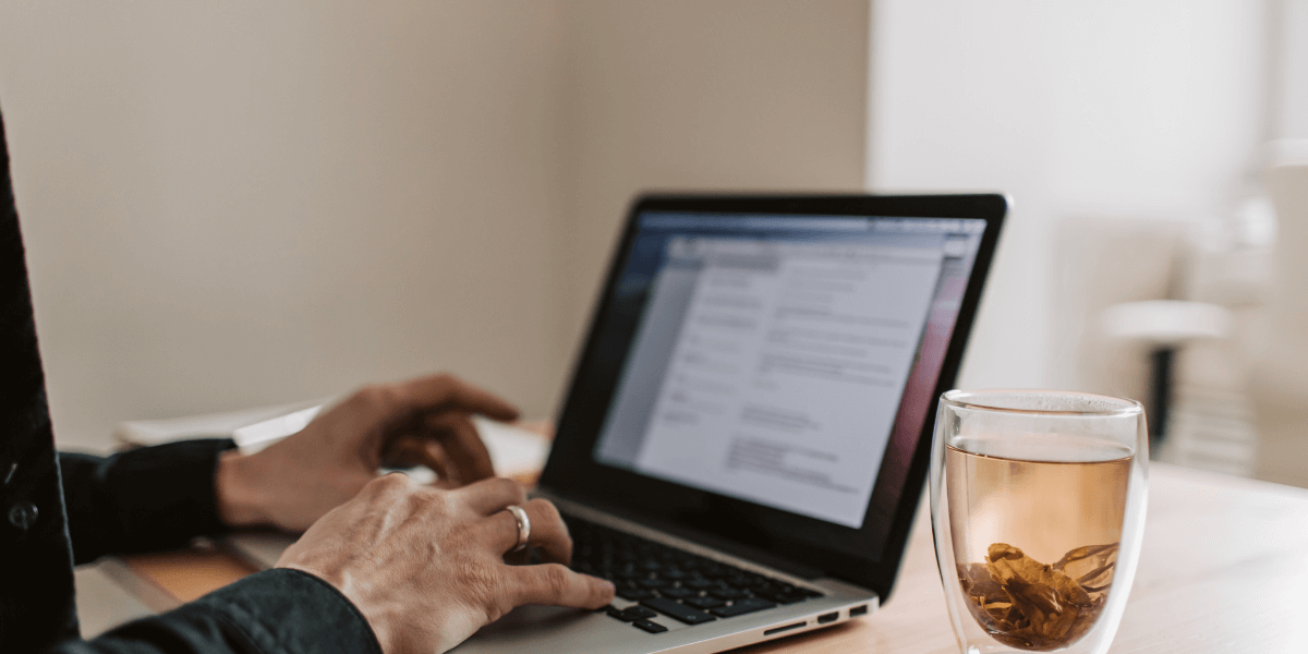 person typing on computer with a cup of tea next to it