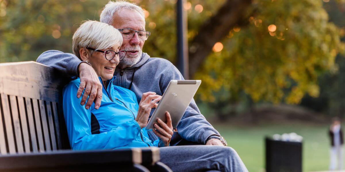 senior couple using tablet on bench