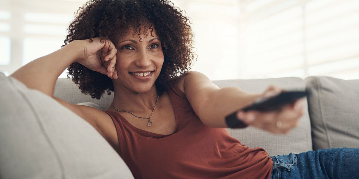 woman sitting on couch smiling with remote