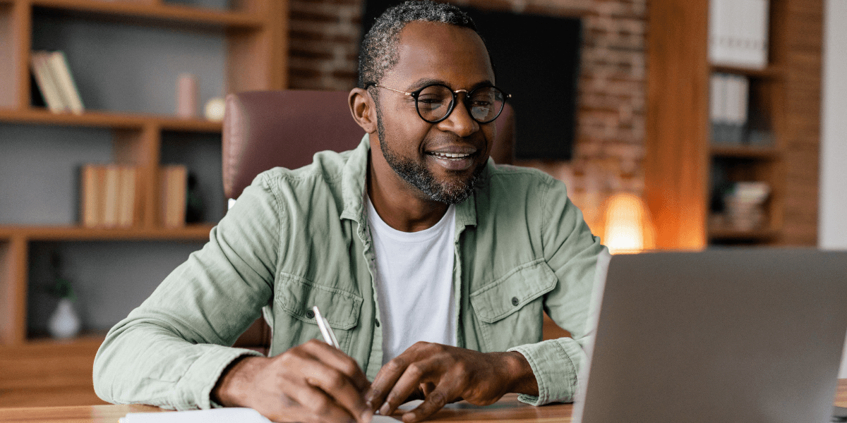 man looking at his laptop taking notes