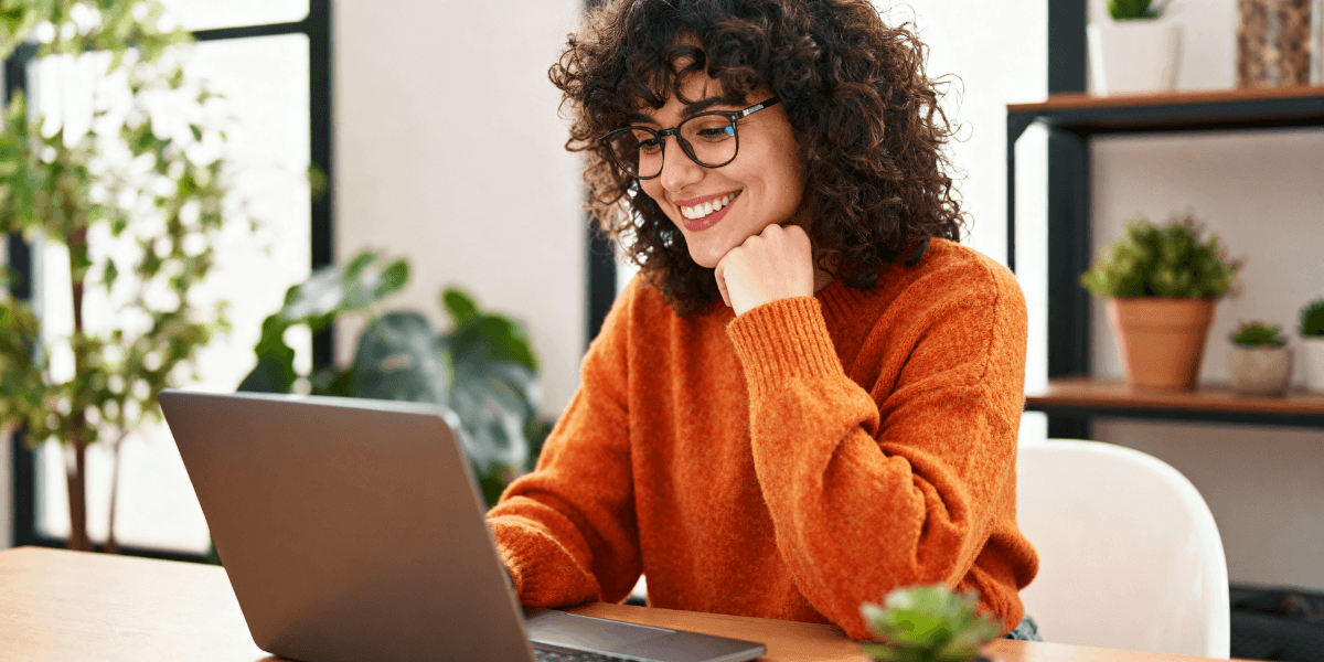 woman in orange shirt looking at laptop