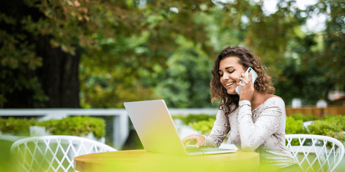 young woman on the phone looking at laptop while outside