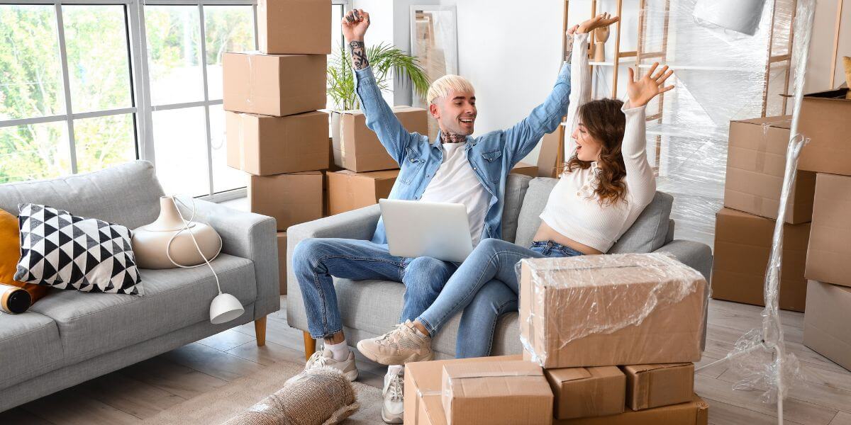 people sitting on a couch with laptop and moving boxes